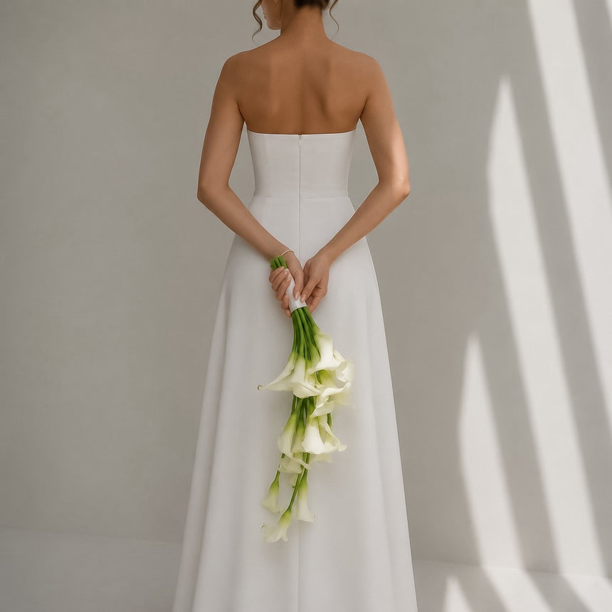 Bride in a modern strapless wedding dress holding the cascading Ivory Falls calla lily bouquet behind her back